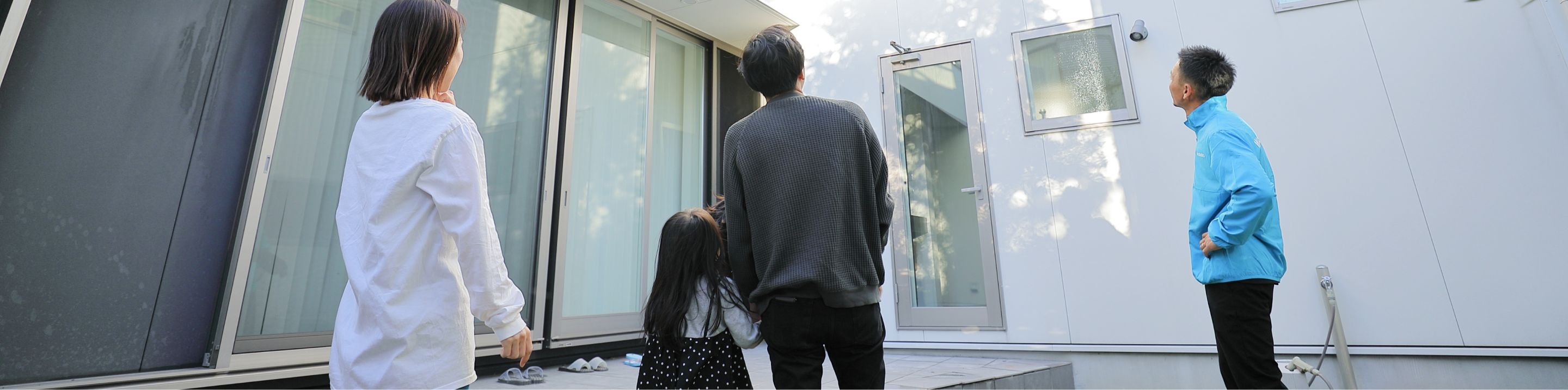 掃除を終えて清潔になった建物を、外壁診断士のスタッフとお客様ご家族が一緒に見上げている様子。